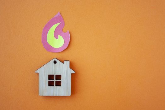 Fire house, insurance and mortgage concept. Small wooden house toy and paper fire shape on orange background top view with copy space