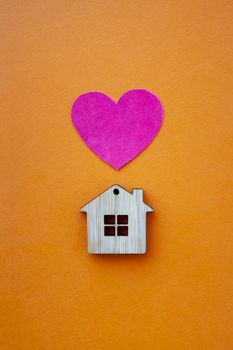 Love home, insurance and mortgage, marriage and valentine concept. Small wooden house toy and paper heart shape on orange background top view 