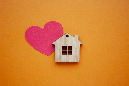 Love home, insurance and mortgage, marriage and valentine concept. Small wooden house toy and paper heart shape on orange background top view 