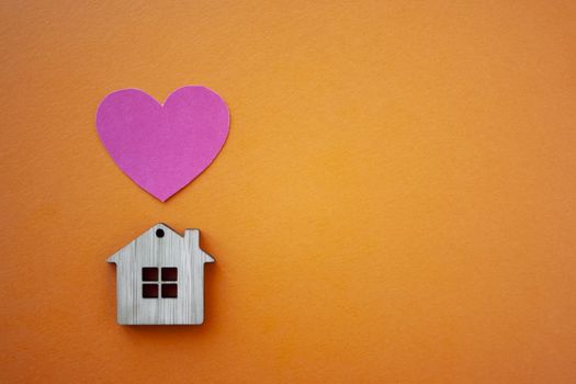 Love home, insurance and mortgage, marriage and valentine concept. Small wooden house toy and paper heart shape on orange background top view copyspace