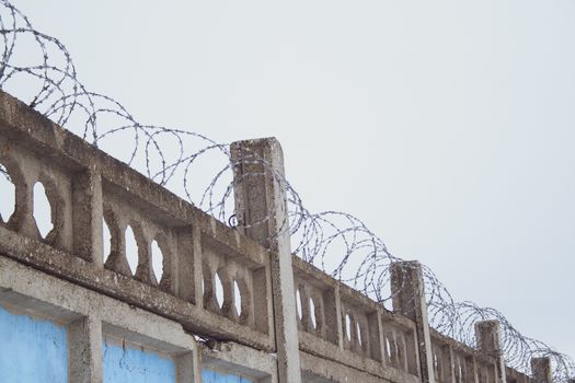 Barbed wires at stone fence on cloudy sky, security, prison concept. 