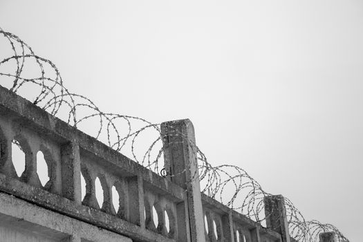 Barbed wires at stone fence on cloudy sky, security, prison concept. 