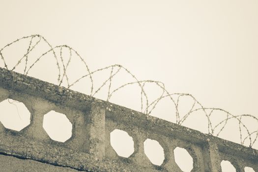 Barbed wires at stone fence on cloudy sky, security, prison concept. 