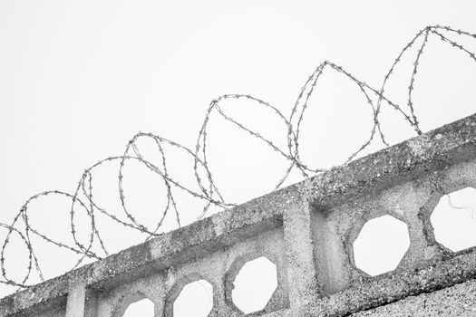Barbed wires at stone fence on cloudy sky, security, prison concept. 