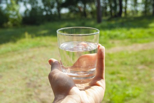 Water glass at man's hand on sunbeams. Hydration at hot summer days concept. Healthy lifestyle symbol. Healthy water drink toned vertical