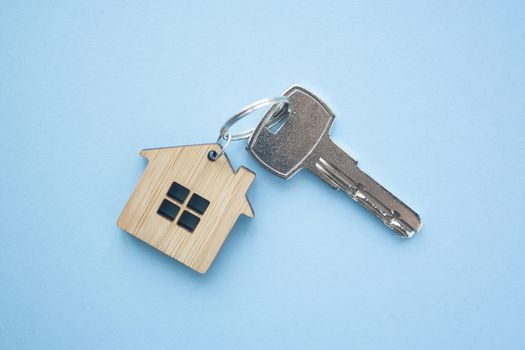 Key and house shaped keychain arrangement on blue background. Top view, flat lay. Real estate, insurance concept, mortgage, buy sell house, realtor concept
