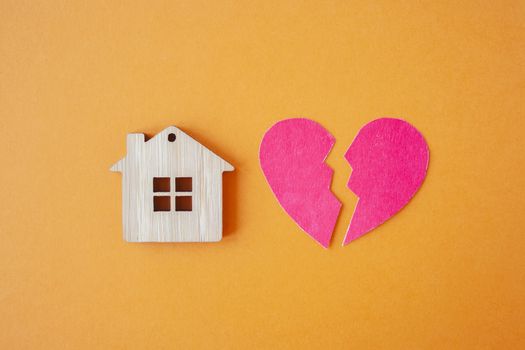 Divorce, division of property, poverty and no money concept. Wooden house with broken heart on bright orange  background. Mortgage, rent, realtor