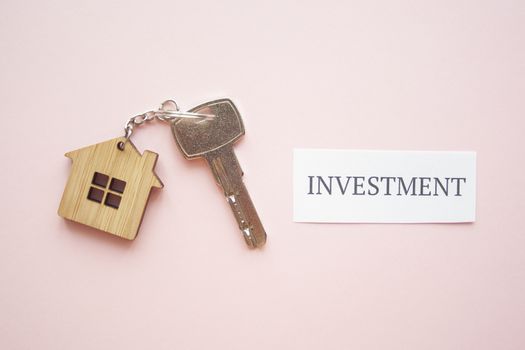 Wooden house toy and silver key on bright pink background with phrase quote Investment. Mortgage, house buy sell, investment, rent, realtor concept