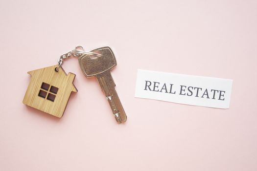 Wooden house toy and silver key on bright pink background with phrase quote Real Estate. Mortgage, house buy sell, investment, rent, realtor concept