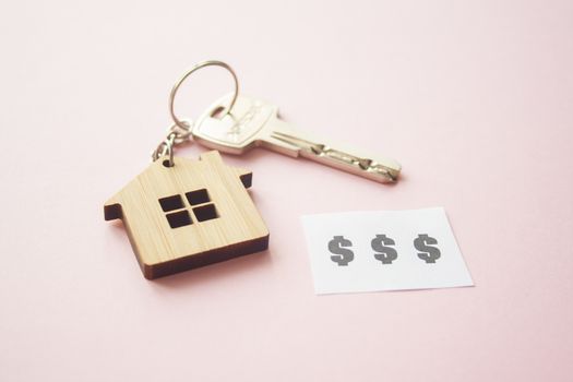 Wooden house toy and silver key on bright pink background with phrase quote $$$. Mortgage, house buy sell, investment, rent, realtor concept