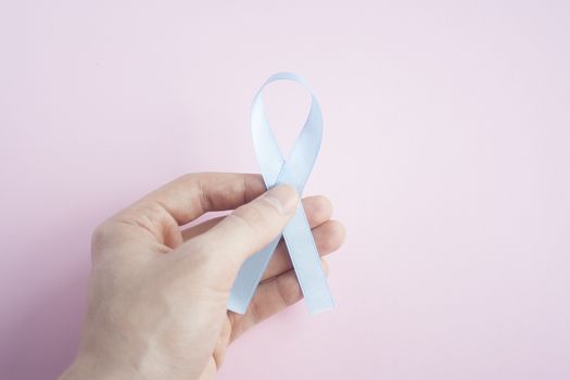 November Prostate Cancer Awareness month, Man Hand holding Blue Ribbon  on pink background for people living and illness. Cancer awareness