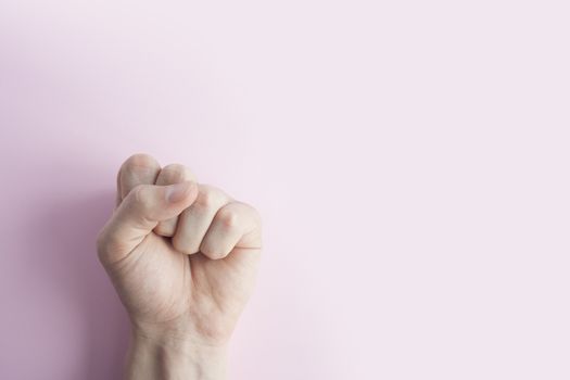 Man's hand with closed fist, on pink background. Copy space Close up. Males hand with a clenched fist 