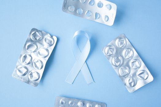 Blue ribbon symbol of prostate cancer with many pills and drugs clusters on bright background. Cancer awareness, cure, treatment concept. Oncology and carcinoma, ribbon