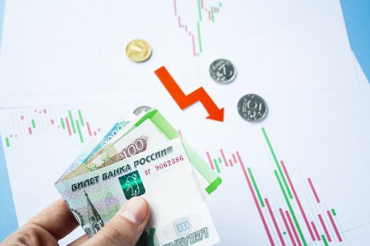 Male hand holding rouble bills on exchange rate of russian ruble and red arrow. ruble depreciation. Exchange rate of rouble fall. Rouble to dollar