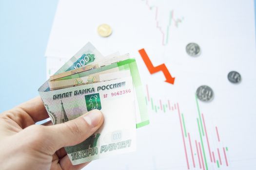 Male hand holding rouble bills on exchange rate of russian ruble and red arrow. ruble depreciation. Exchange rate of rouble fall. Rouble to dollar