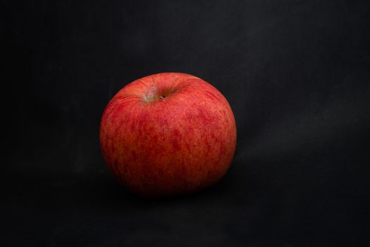 A fresh red apple with droplets of water against black background with space for text