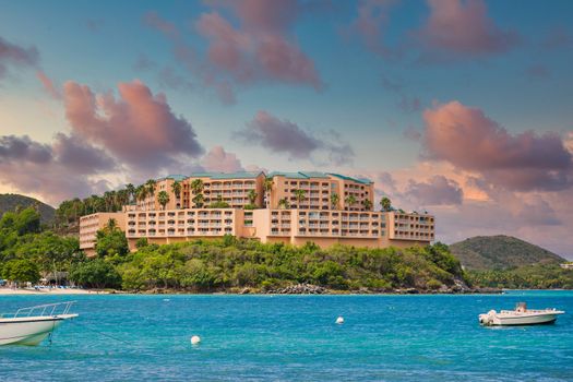 Boats anchored in blue bay by peach colored luxury resort on a lush green island