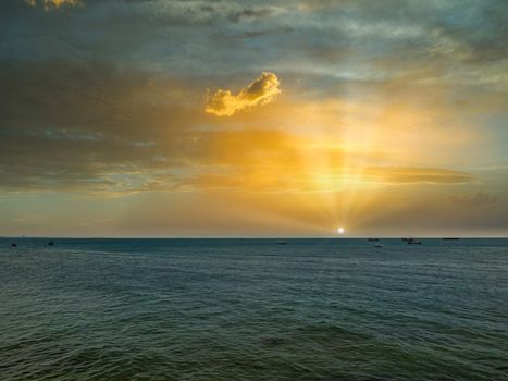 The sun rises above the sea on a bright morning, with fishing boats anchored after returning from fishing.