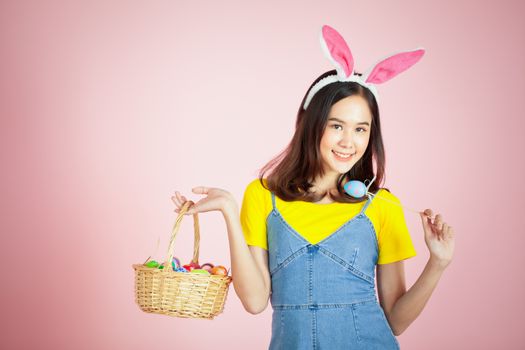 Portrait of a happy young woman wearing Easter bunny ears prepares to celebrate Easter on a pink background.