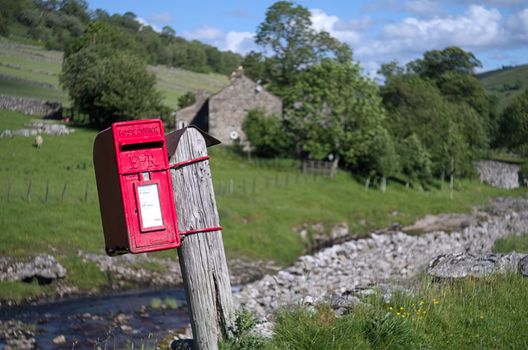 Red postbox clinging to a wooden post by the side of a country road in the Yorkshire Dales.