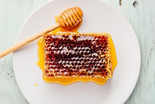 Top view of delicious yummy honeycomb on bright plate with honey dipper over light wooden background