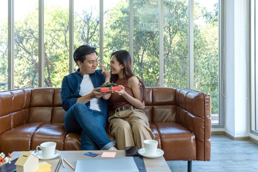 Young couples spend holidays in the living room. The young man wears comfortable clothes, hand a gift box  to surprise girlfriend on special occasions.