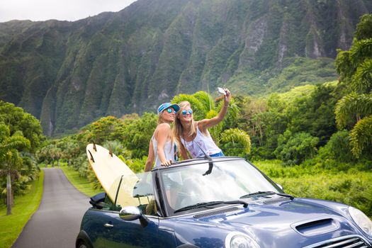 Car Road Trip vacation young people taking selfie photo with phone during summer travel vacation. Tourists couple taking photos on Hawaii in convertible car, with smartphone camera