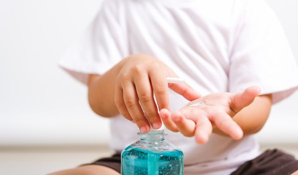 Closeup Asian little child boy sitting applying bottle pump dispenser sanitizer alcohol gel cleaning washing hands yourself, COVID-19 or coronavirus protection concept, isolated on white background with copy space