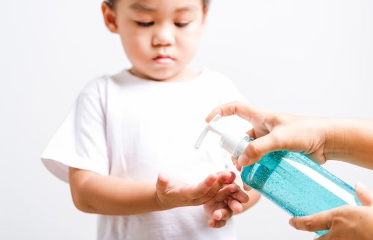 Closeup Asian Mother applying bottle pump dispenser sanitizer alcohol gel cleaning washing hands little child boy COVID-19 or coronavirus protection concept, isolated white background with copy space