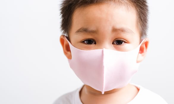 Portrait Asian little child boy wearing cloth face mask protective filter dust pm2.5, COVID-19 or coronavirus concept he looking to camera, studio shot isolated on white background with copy space