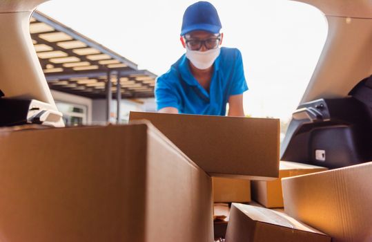 Asian delivery man courier moving deliveries out boxes in back car he protective face mask, service customer on front house under curfew quarantine pandemic coronavirus COVID-19, in car trunk view