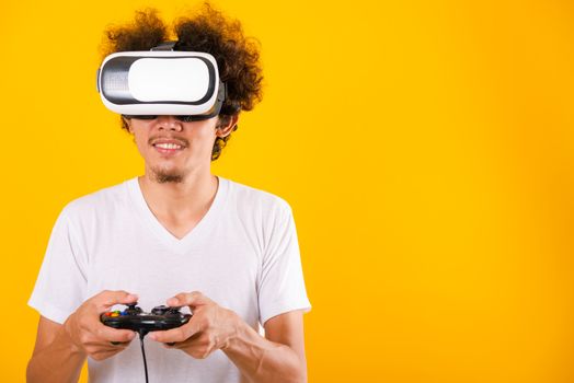 Asian handsome man with curly hair play game he using virtual reality headset or VR glass isolate on yellow background with copy space for text