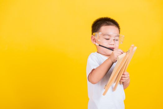 Asian Thai happy portrait cute little cheerful child boy smile are drawing on blackboard and looking the board, studio shot isolated on yellow background with copy space