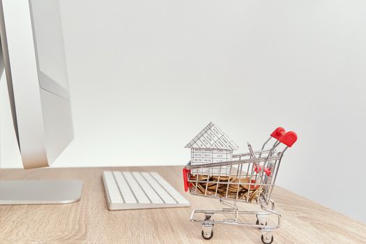 House on gold coins in shopping cart on wooden computer table with white background and copy space. Business and finance concepts shopping online photography.