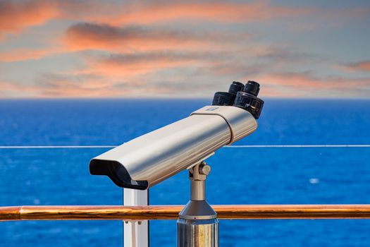 A silver spotting scope on the deck of a ship overlookng blue seas