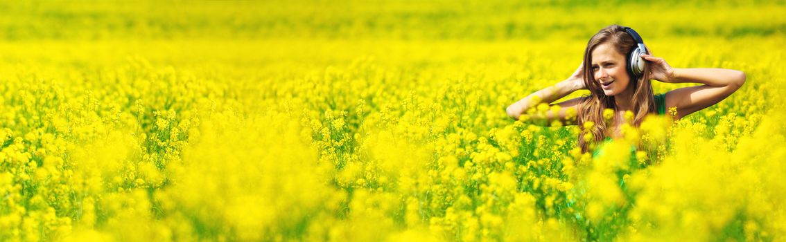 Young woman with headphones listening to music on oilseed flower field