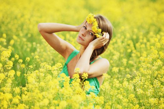 Pretty happy woman in dandelions wreath enjoy nature, happy cheerful girl resting on oilseed field