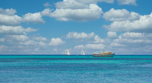 White and yellow fishing boat and two white sailboats on calm blue sea