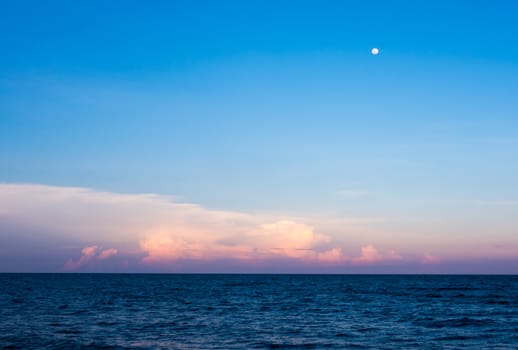 Pink Clouds and moon in sunset sky over sea