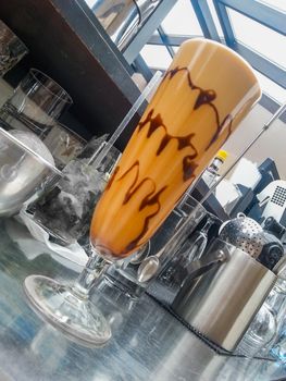 Iced coffee in high glass with chocolate decoration behind bar