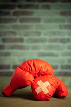 Red boxing gloves on wooden table and brick wall at the sport gym. Adhesive plaster across each other on boxing gloves. Idea of getting hurt or combat losing business rival. Fighting giving up boxing