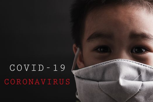 Closeup Asian little child wearing protective face mask with fear in the eye, prevent germs or disease hygiene prevention COVID-19 virus or coronavirus protection concept, dark on black background