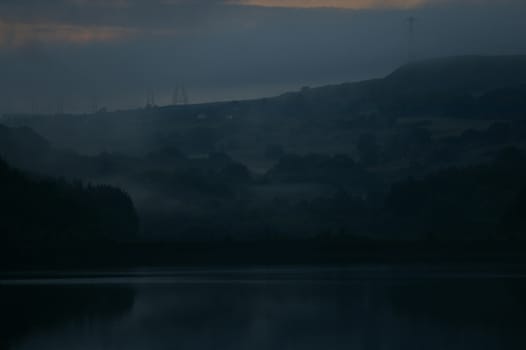 Brooding, dark view of Wayoh Reservoir in Lancashire on a misty dusk evening