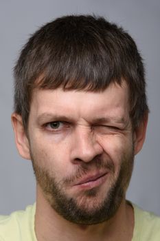 Close-up portrait of a man of European appearance who squeezed his right eye tightly