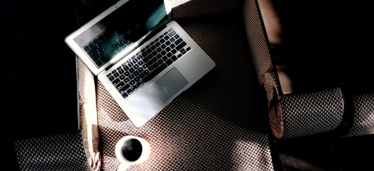 Laptop and mug of steaming coffee on the couch in the light of the morning sun