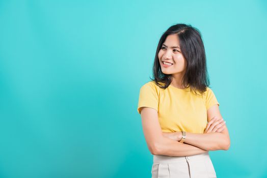 Portrait Asian beautiful happy young woman smiling wear yellow t-shirt standing cross arm with looking side away at copy space, shoot photo in a studio on a blue background