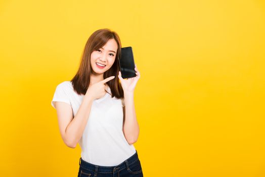 Asian happy portrait beautiful cute young woman smile standing wear t-shirt making finger pointing on smartphone blank screen looking to camera isolated, studio shot yellow background with copy space