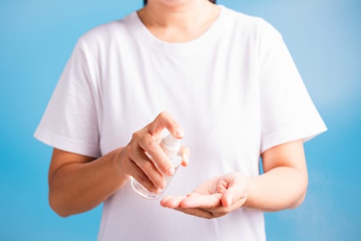 Closeup Hand Asian young woman applying spray pump dispenser sanitizer alcohol on hand wash cleaning, hygiene prevention COVID-19 or coronavirus protection concept, isolated on blue background