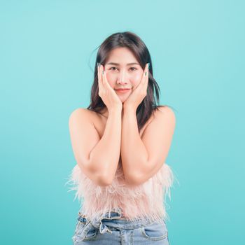 Asian happy portrait beautiful young woman standing smiling surprised excited her hands over her face and looking to camera on blue background with banner copy space for text