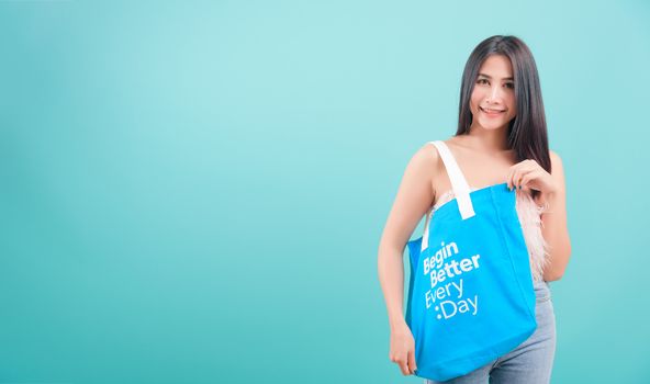 Asian happy portrait beautiful young woman standing smile her holding eco fabric cotton bag on hand and looking to camera on blue background with copy space for text
